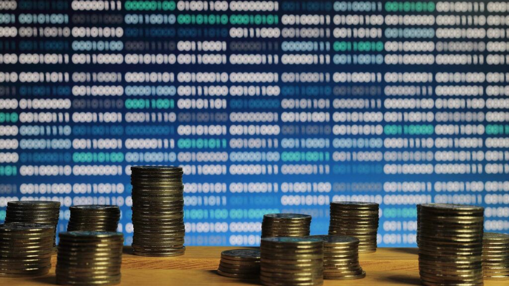 Piles of coins in front of blue binary code computer screen