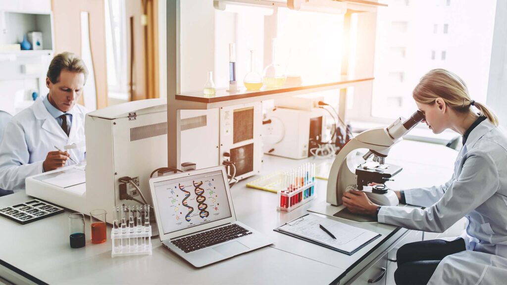 Man and woman working in a laboratory, looking at a computer and microscope