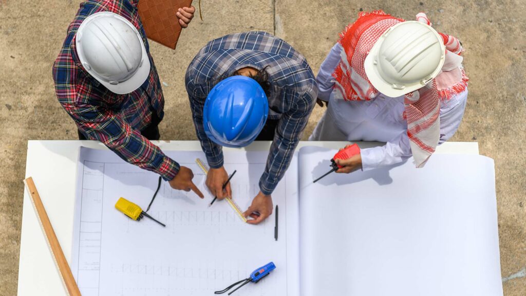 Overhead view of 3 engineers looking over project plans